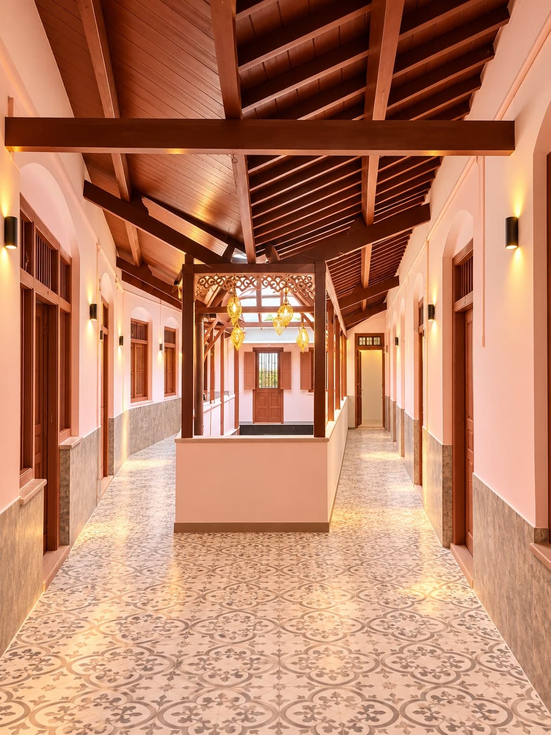 Guest passage with exposed wooden roof beams, arched wall niches, patterned floor tiles and hanging brass lanterns